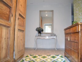 Un pasillo con una puerta de madera, una consola con un florero, un espejo y un aparador de madera.