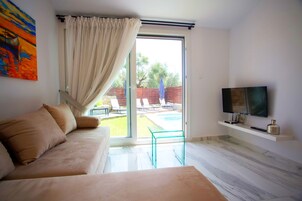 Un dormitorio moderno con sofá, televisor en un estante y puerta de cristal corredera que da a una zona de piscina.