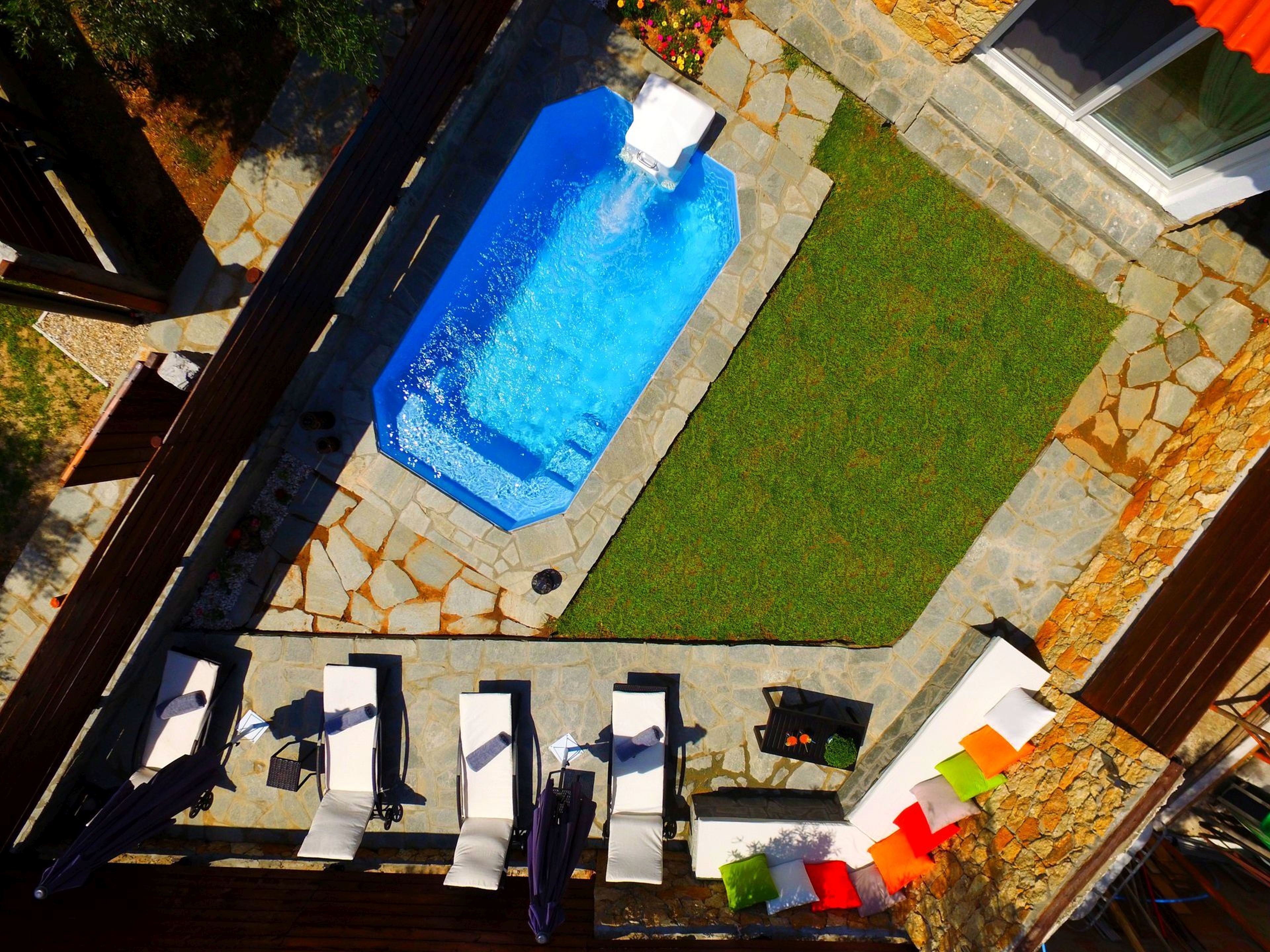 Luftaufnahme eines Hinterhofs mit Swimmingpool, Stein-Terrasse und Liegestühlen.
