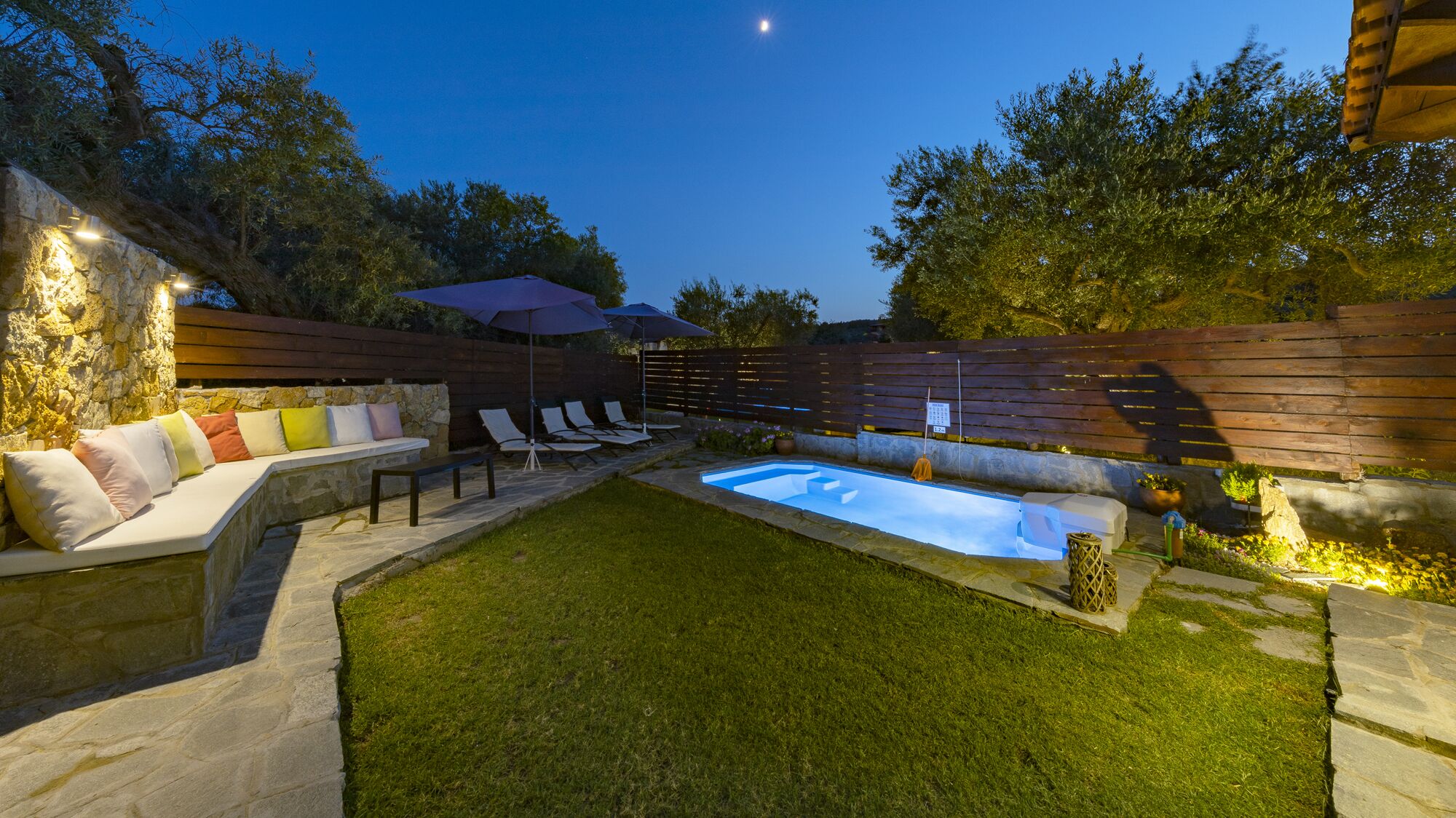 A backyard with a swimming pool, stone seating, and a wooden fence.