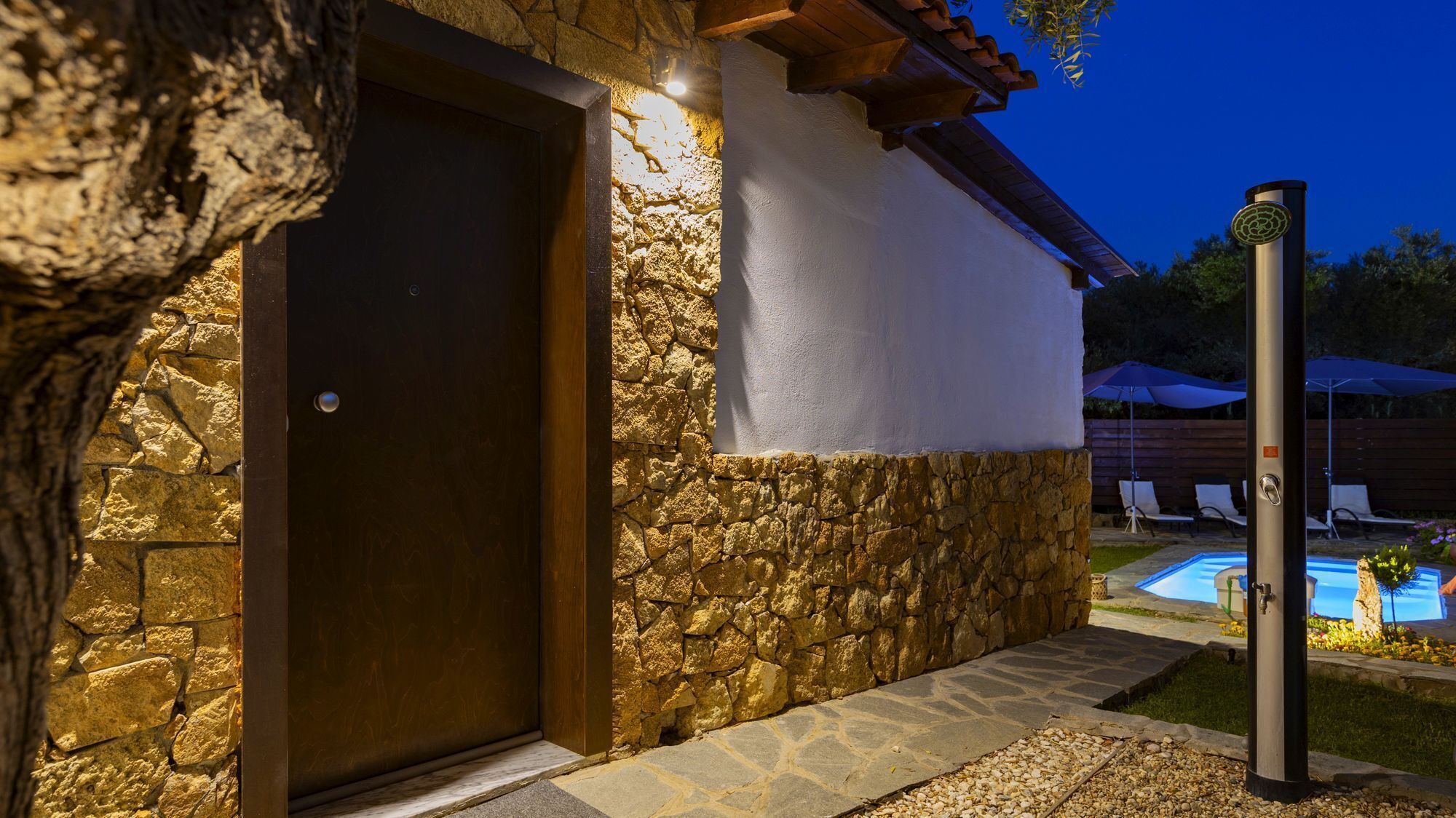 A stone exterior with a wooden door, a swimming pool, and a covered patio area.