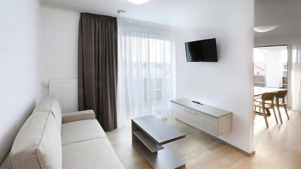 En moderne stue med sofa, sofabord, TV og et spiseområde med stole.