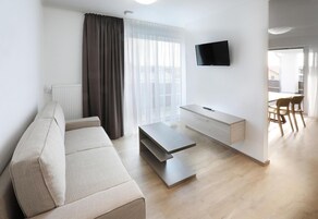 Uma sala de estar moderna com um sofá, uma mesa de centro, uma televisão e uma área de jantar com cadeiras.