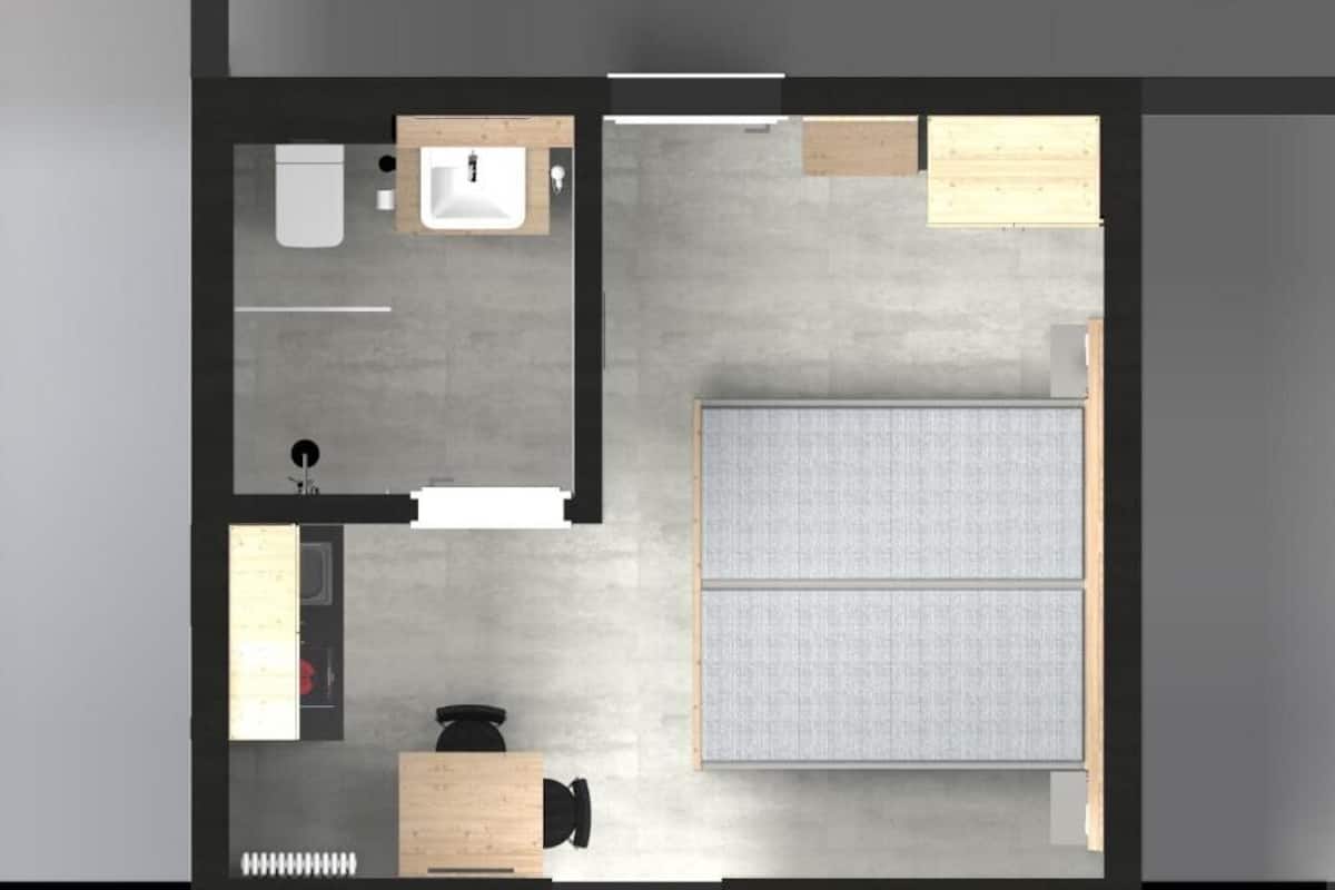 Ein modernes Hotelzimmer mit Bett, Schreibtisch, Stuhl, einem kleinen Tisch, einem Schrank, einem Badezimmer mit Toilette und Waschbecken sowie einem Spiegel.