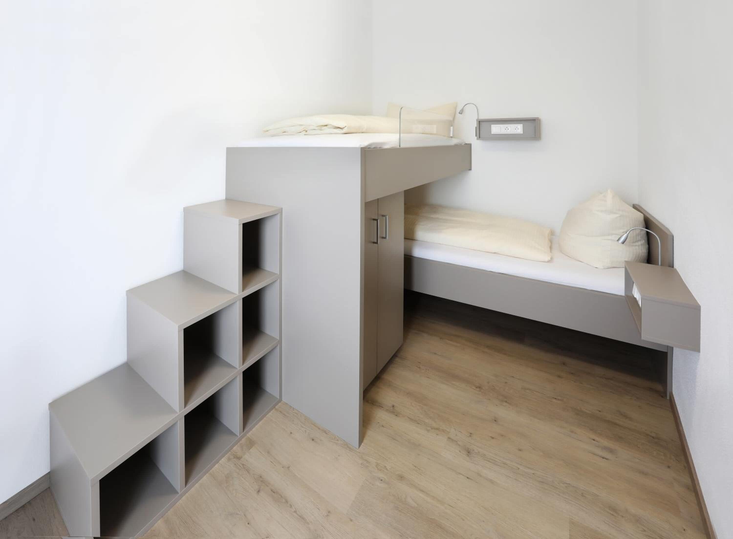 A compact room with a bunk bed, built-in shelving, and a bedside table.