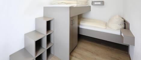 Una habitación compacta con literas, estantes empotrados y una mesita de noche.