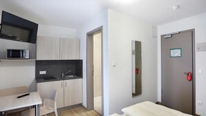 Et lille hotelværelse med tekøkken, seng, skrivebord og stol.