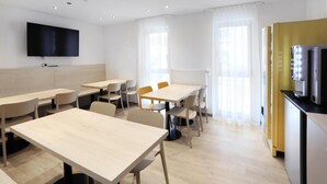 Et moderne hotelværelse med et stort fladskærms-tv, flere siddeområder med borde og stole, og et tekøkken med en mikrobølgeovn.