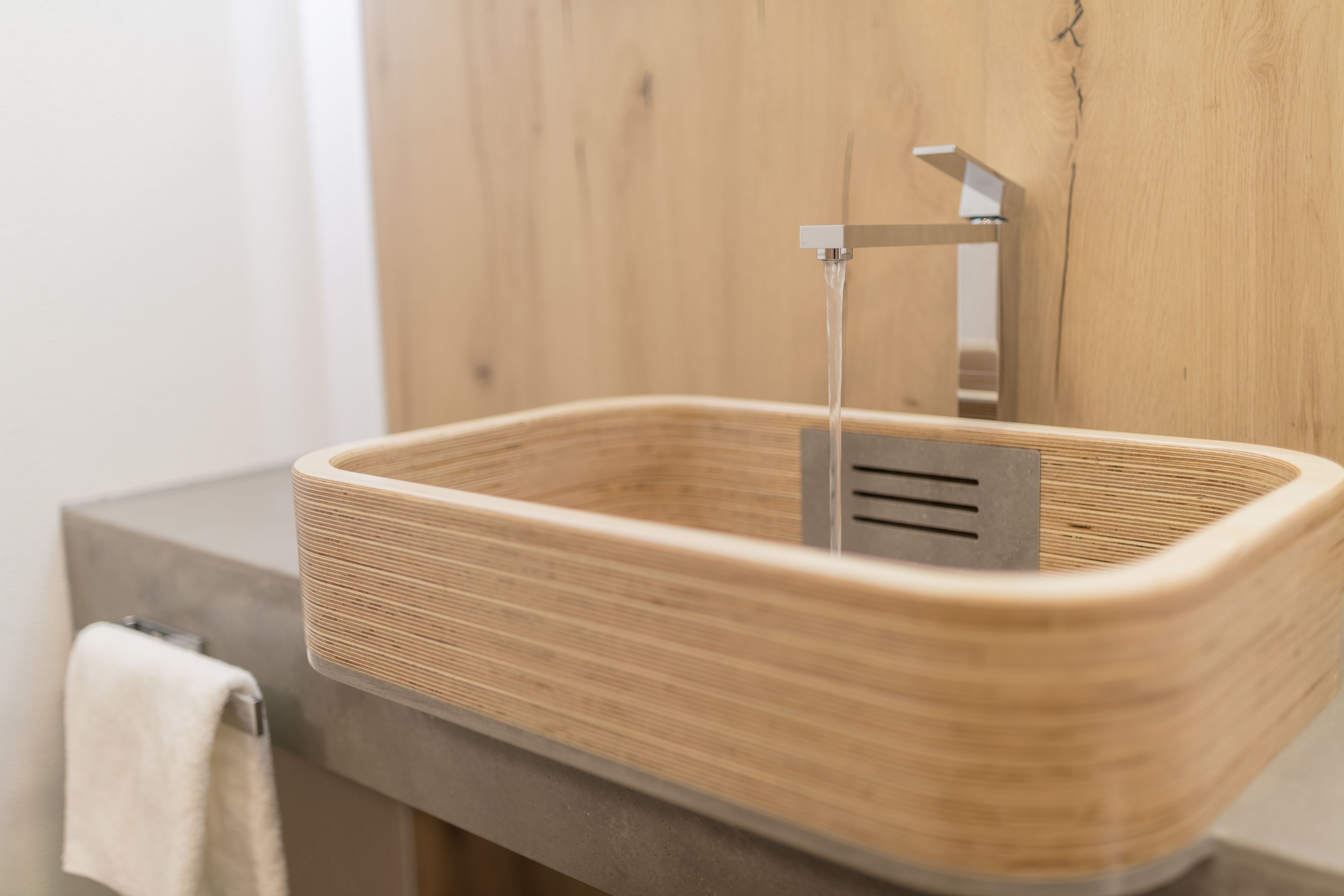 A modern bathroom with a wooden sink, a towel rack, and a wooden wall.