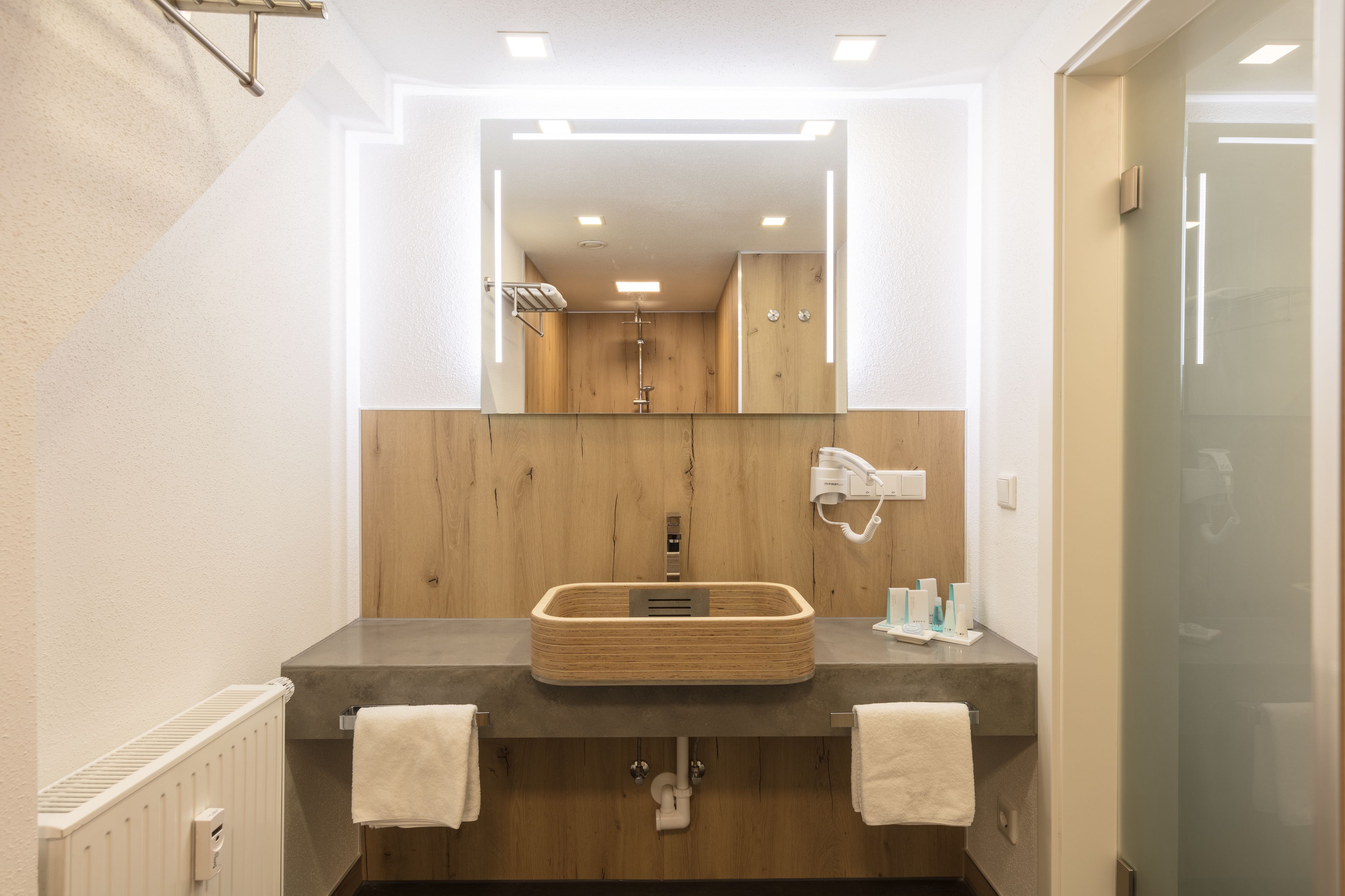 A modern bathroom with a wooden vanity, a large mirror, and a towel rack.
