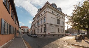 A historic building with a classic architectural style, featuring a prominent entrance and a cobblestone street in front. - Luxus Hostel Rabe Mühlhausen (Muhlhausen/Thuringen)
