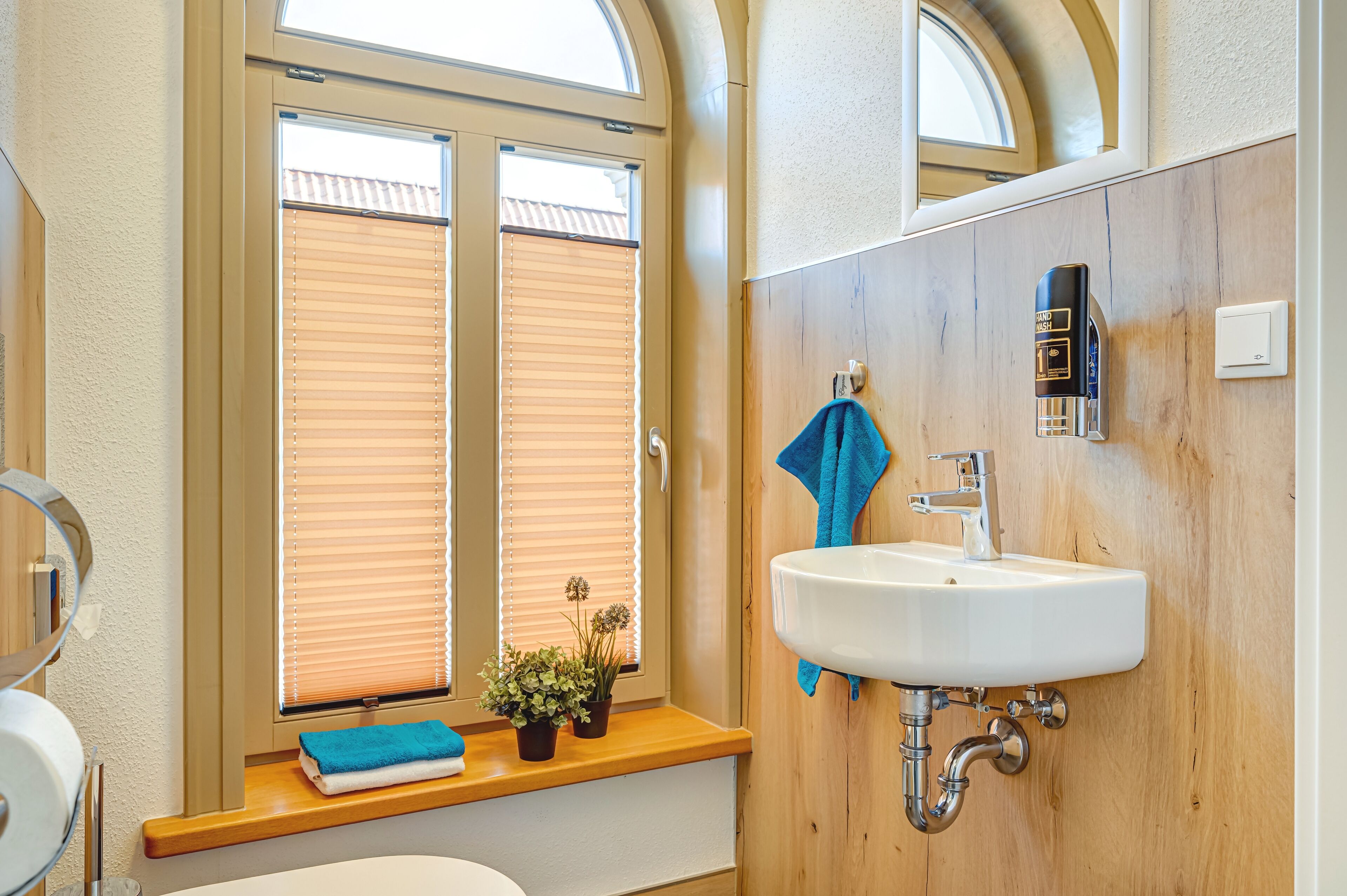 Un baño con tocador de madera, un lavabo blanco, un perchero para toallas y una ventana con persianas.