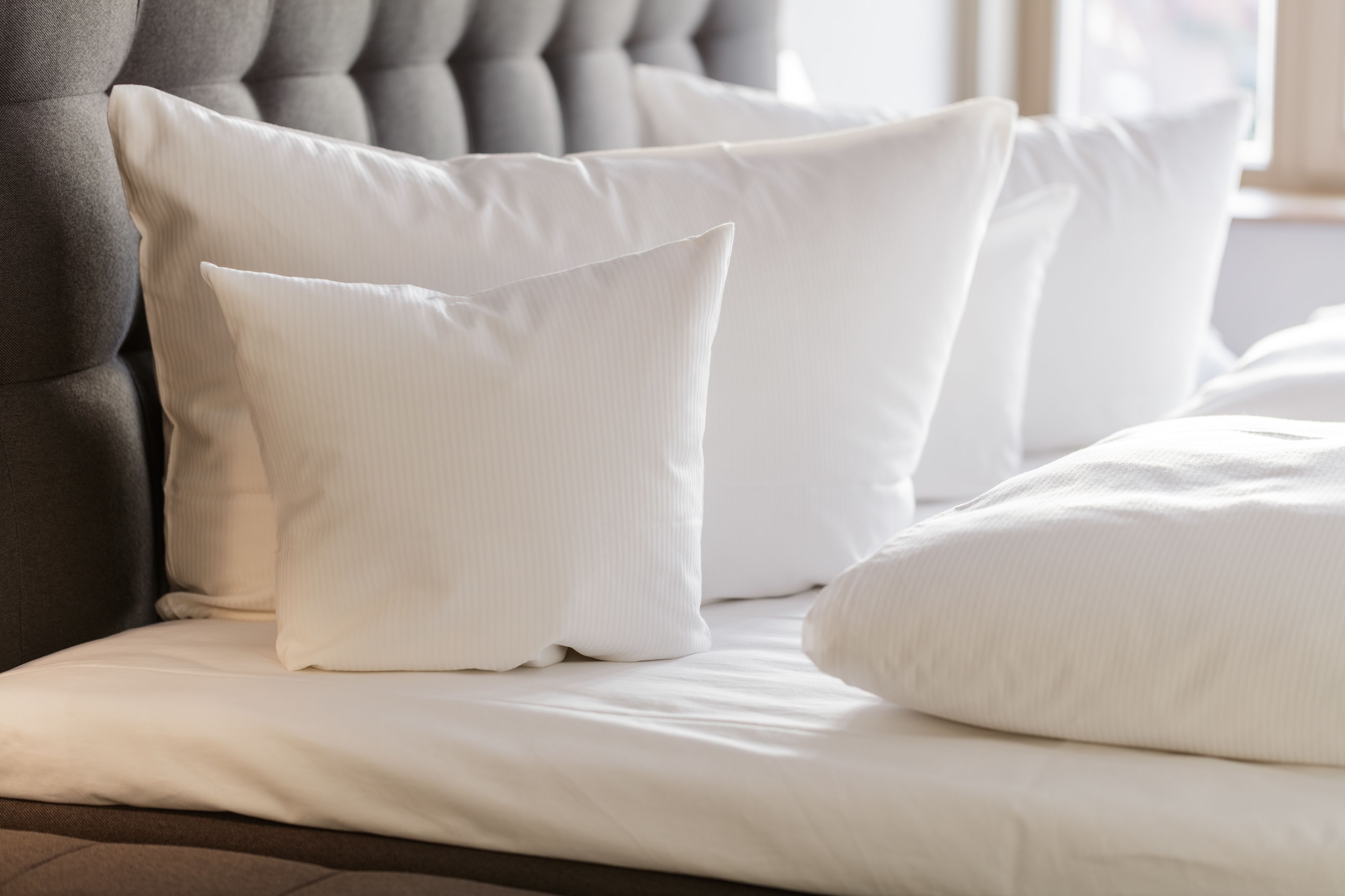 Un letto rifatto con cura, lenzuola e cuscini bianchi, una testiera trapuntata e una finestra sullo sfondo.