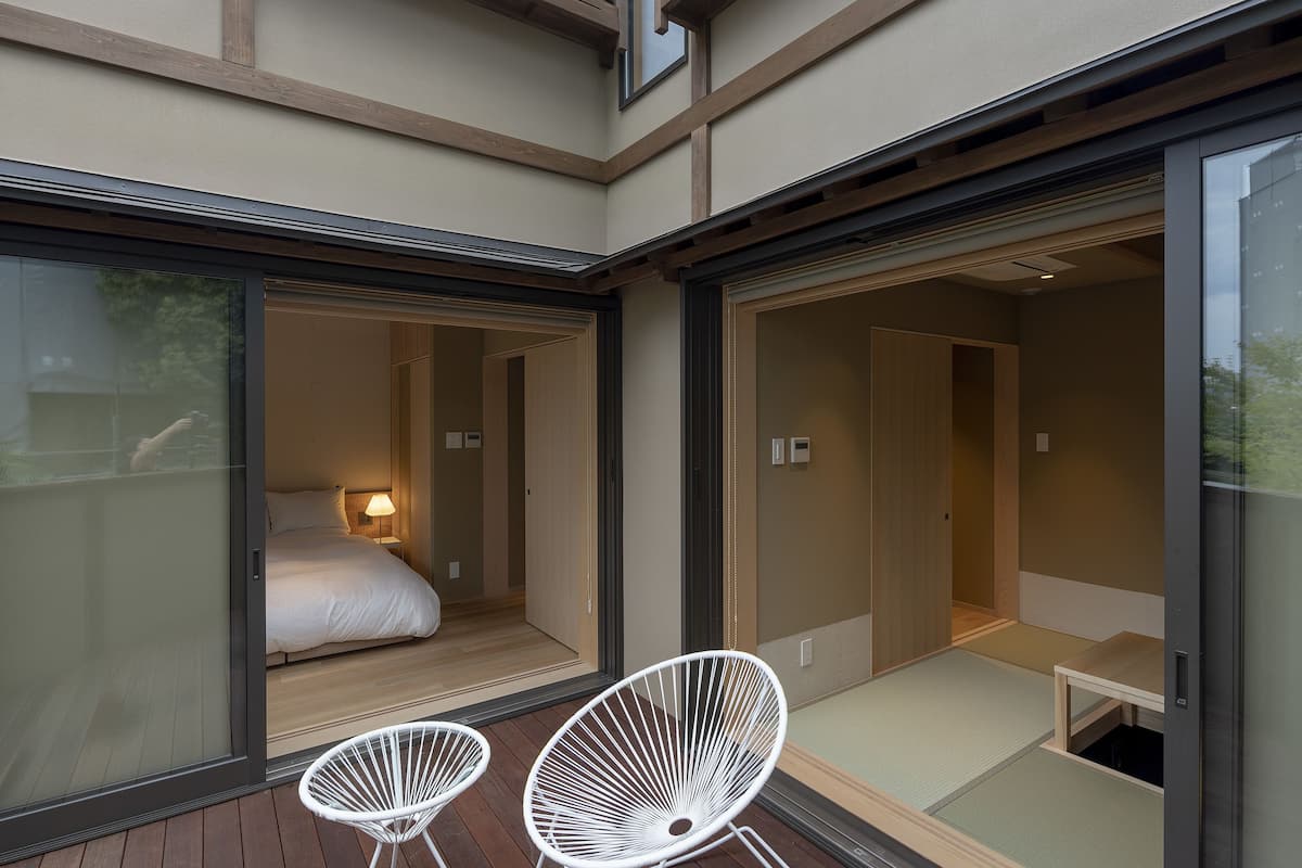 A modern interior with a wooden deck, two white wire chairs, and a bed with a nightstand.