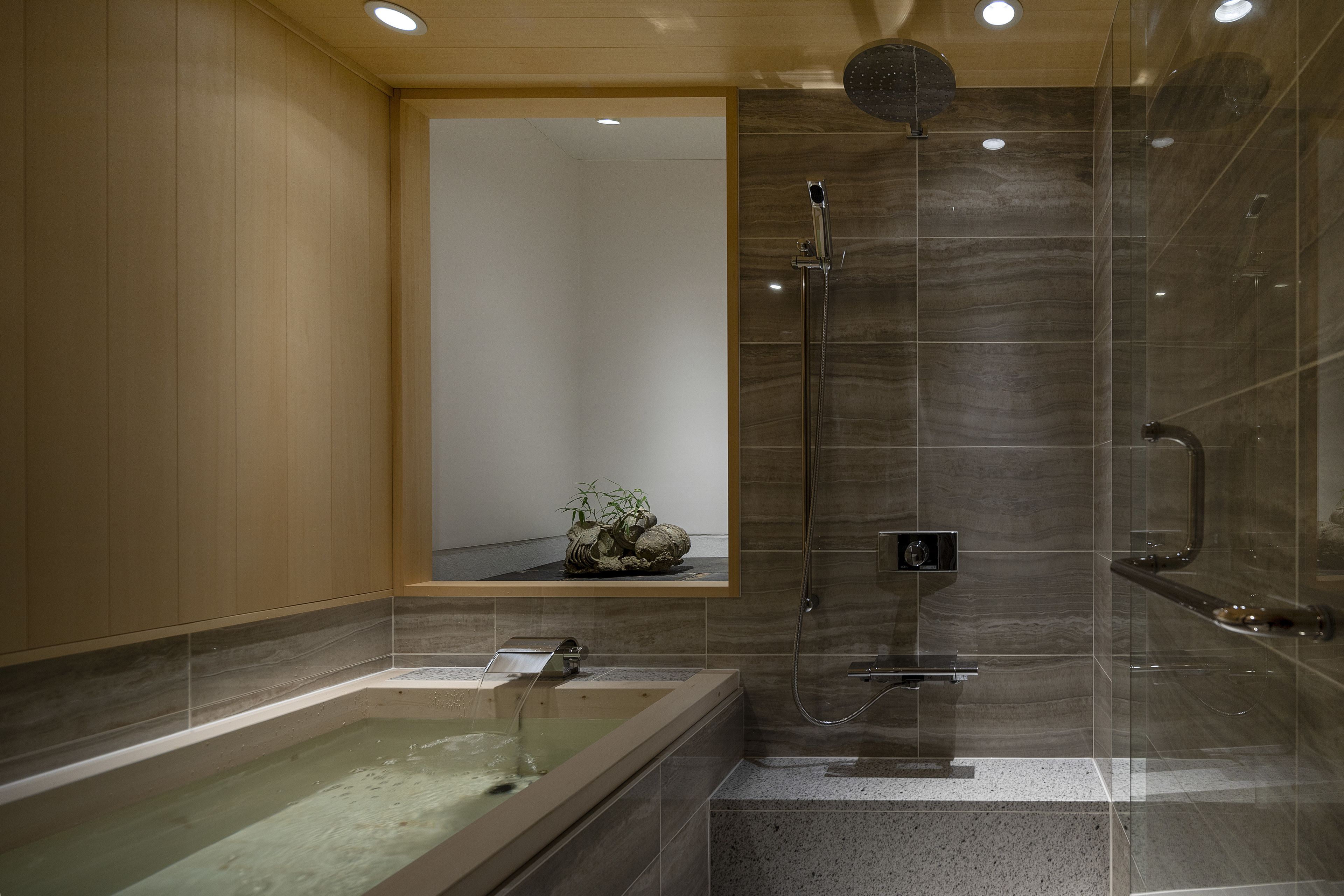 A modern bathroom with a glass-enclosed shower, a freestanding bathtub, and a small shelf with decorative items.