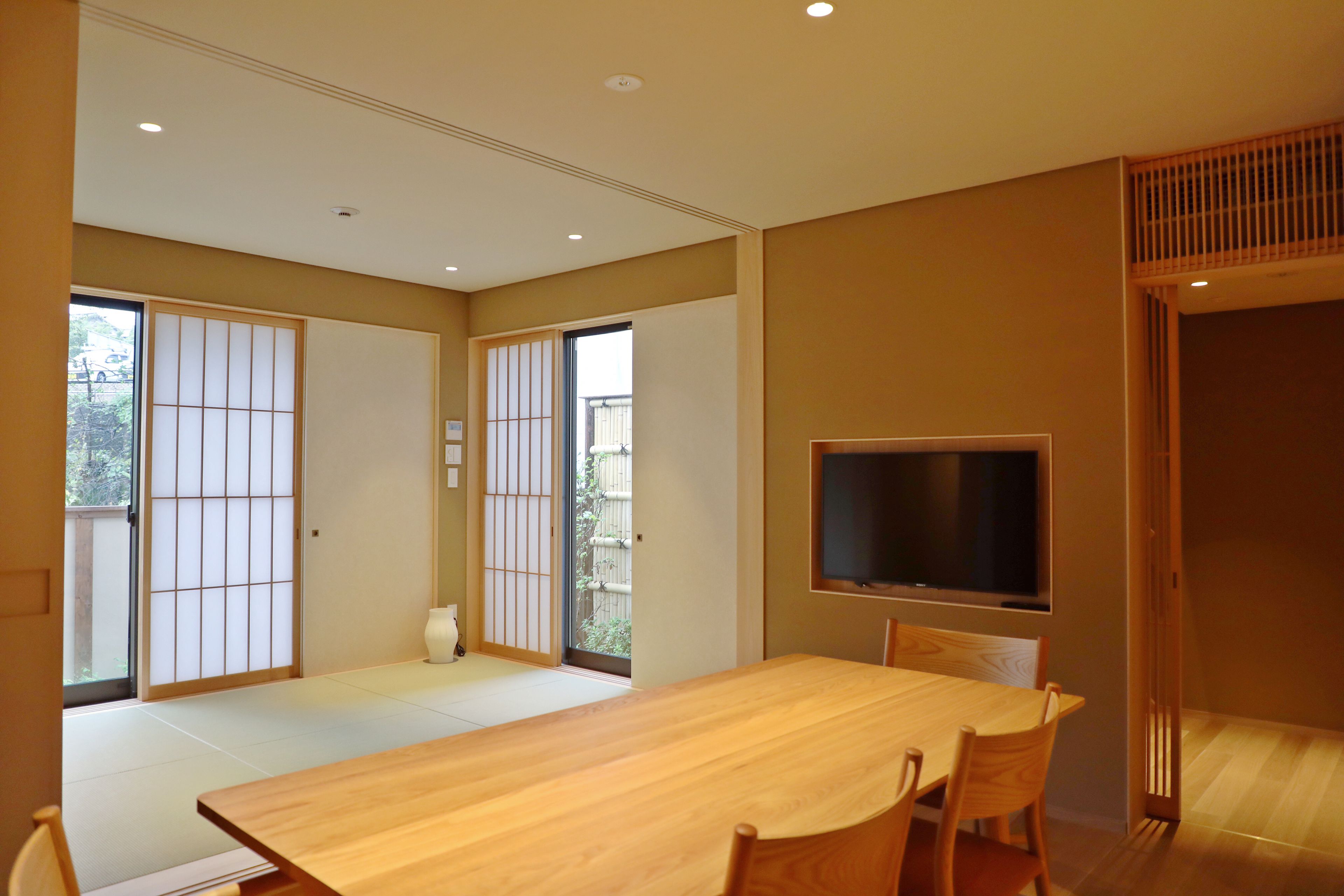 A spacious room with a large wooden dining table, sliding doors, and a mounted television.
