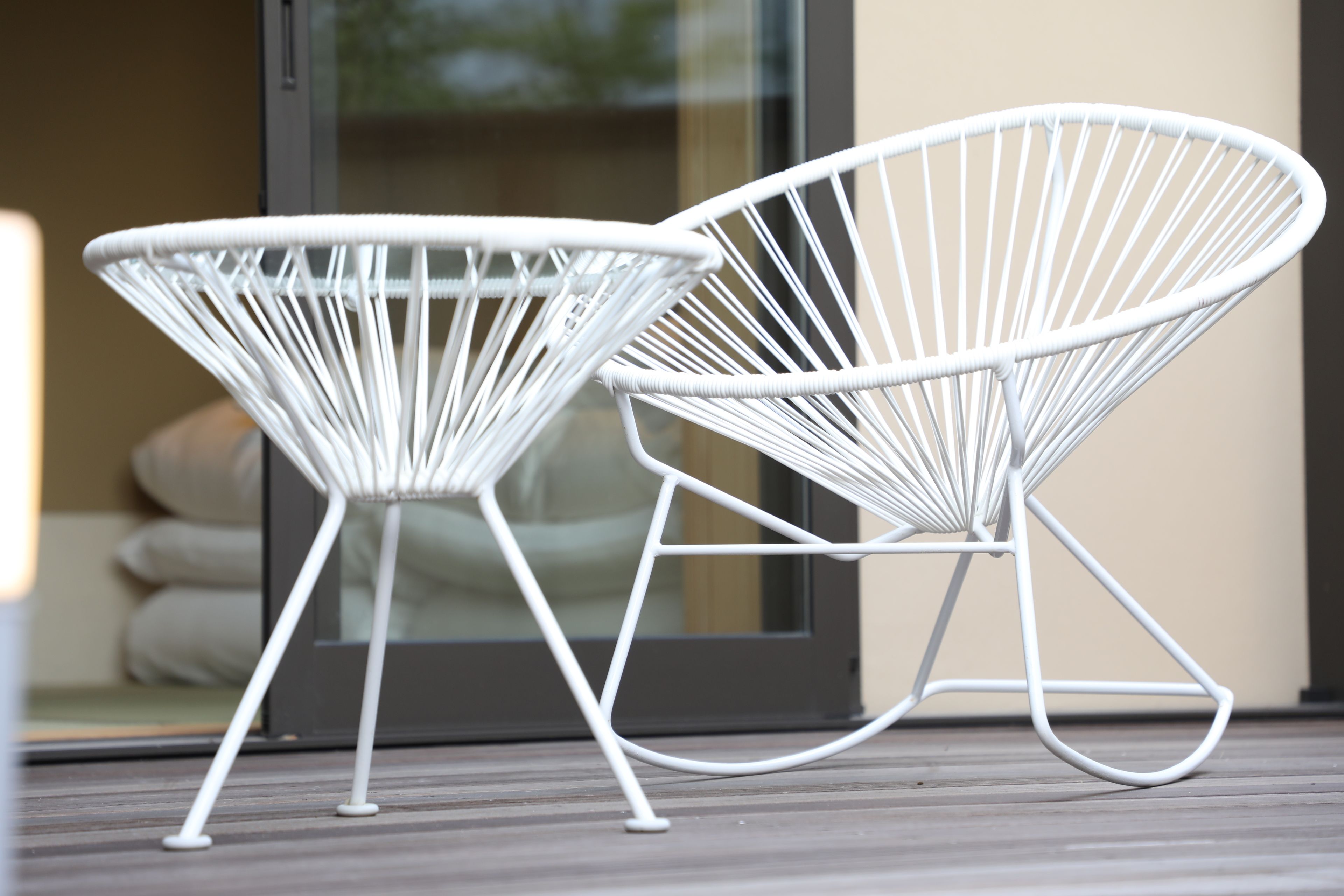 Dos sillas con estructura de alambre blanco sobre una terraza de madera.