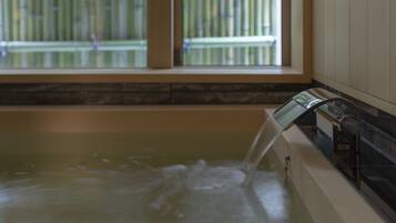 A bathtub with running water, a window with a view of a bamboo fence, and a stone countertop.