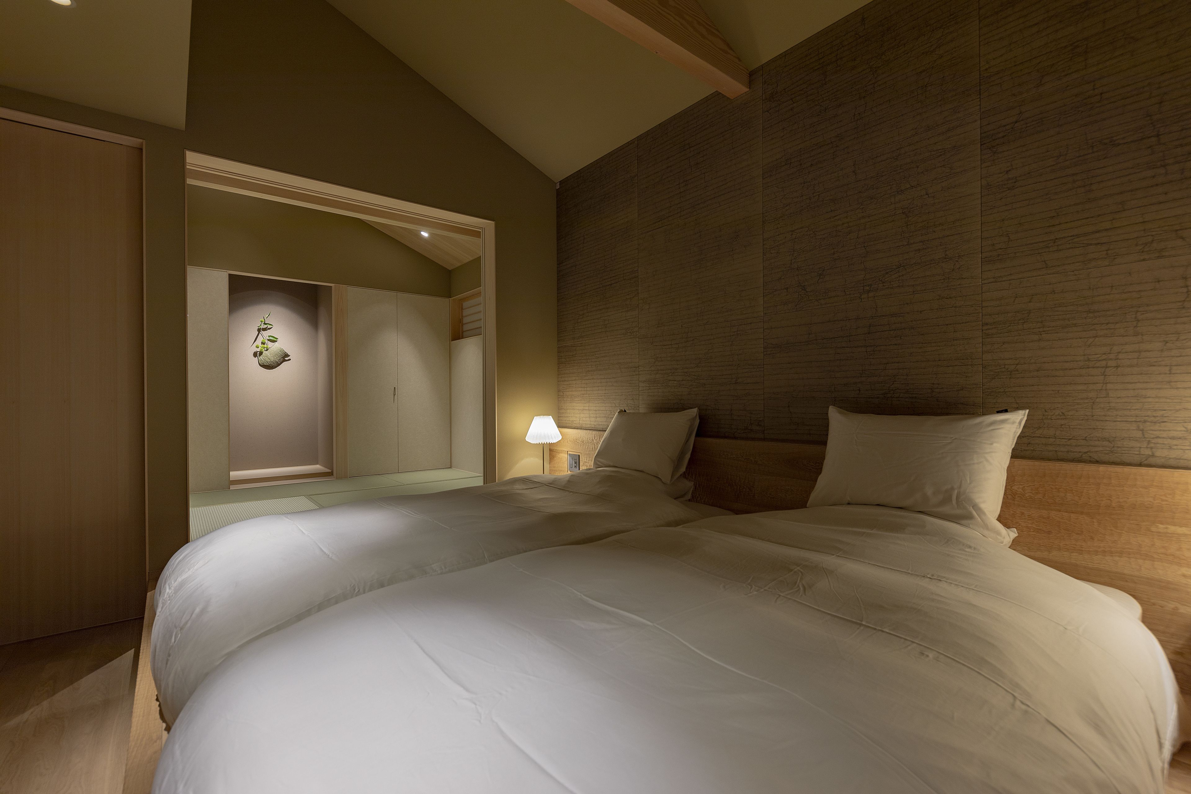 A bedroom with a large bed, a nightstand with a lamp, a wooden headboard, and a wardrobe.