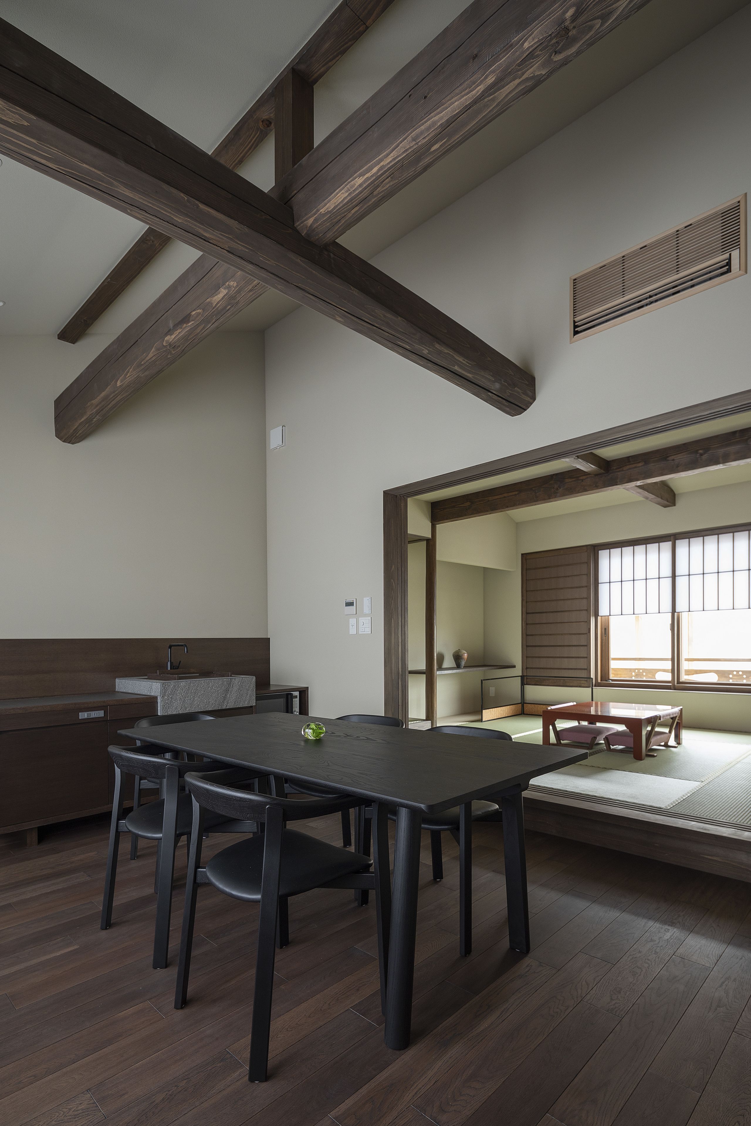 A dining area with a wooden table and chairs, a bench, and a view of a traditional Japanese room.