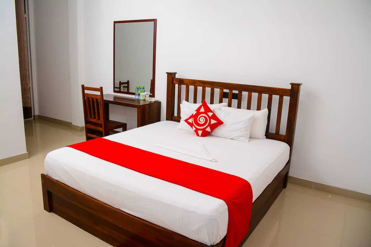 A neatly made bed with a red blanket, a wooden headboard, and a single red pillow.