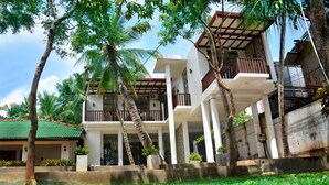 A modern multi-story building with balconies, surrounded by lush greenery and palm trees. - Sea View Tourist Inn (Tangalle)