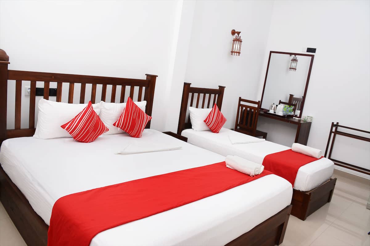 A hotel room with two beds, each with white bedding and red accents, a wooden headboard, and a small bedside table with a mirror and toiletries.