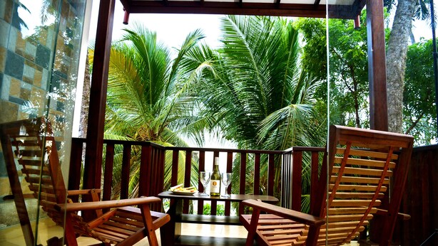 A wooden deck with a table and chairs, overlooking a lush garden with palm trees. - Sea View Tourist Inn (Tangalle)