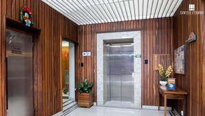 Een receptiegedeelte met houten lambrisering, een service lift, een potplant en een kleine tafel met een bordje.