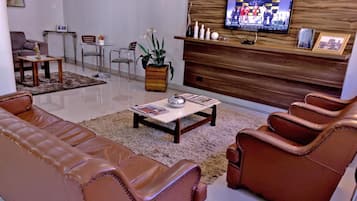 A modern living room with leather sofas, a coffee table, and a TV mounted on a wooden wall.