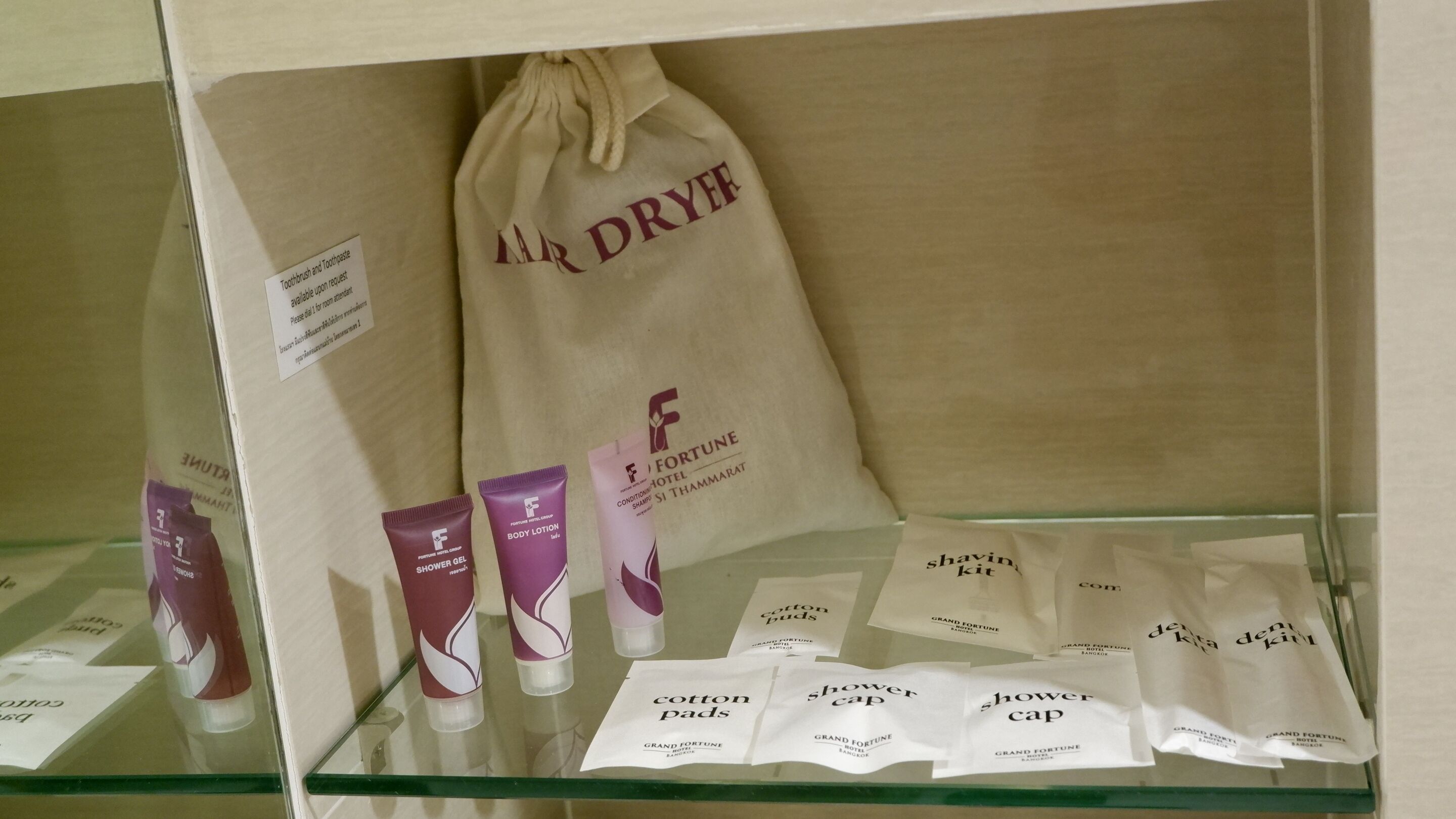 Eine Auswahl an Hotelausstattung, darunter eine Tasche mit Kordelzug mit dem Aufdruck 'LAR DRYER', Körperlotion, Duschgel, Wattepads und Duschhauben.