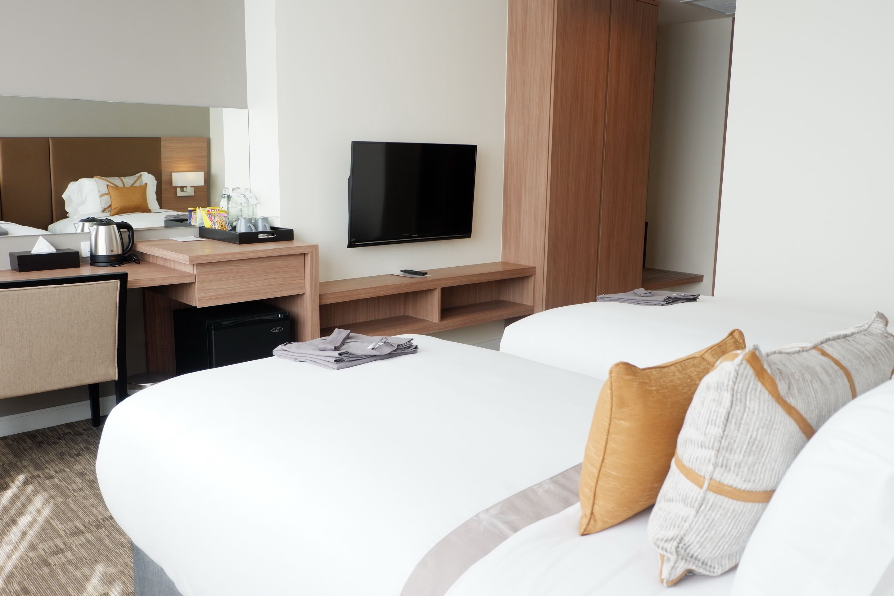 A hotel room with a bed, a desk with a flat-screen TV, a coffee maker, and a mirror.