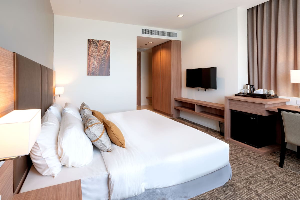 Quarto de hotel com uma cama grande, uma escrivaninha com televisão de tela plana, uma cadeira e uma kitchenette pequena.