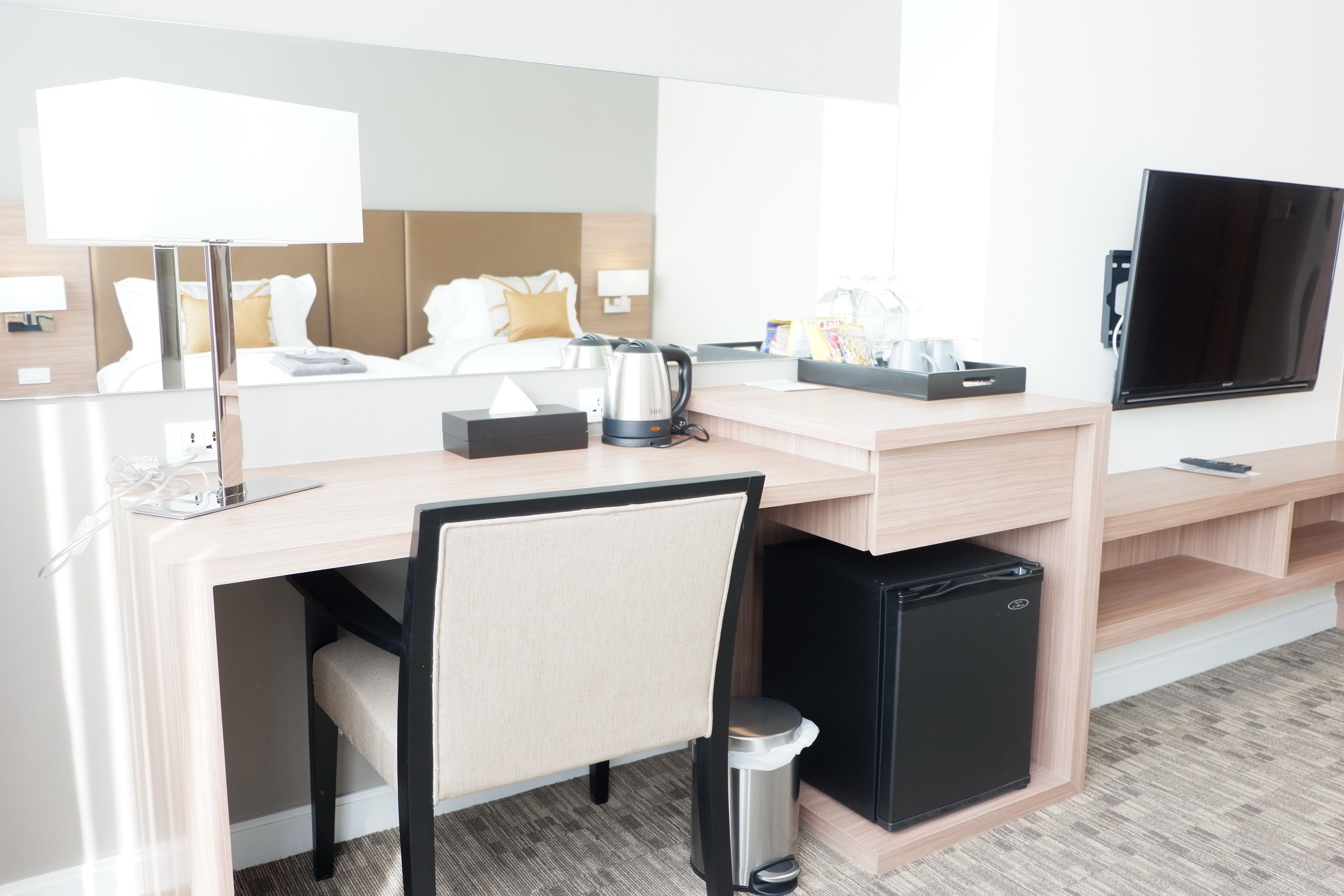 A hotel room with a desk, chair, television, and a bed with a headboard.