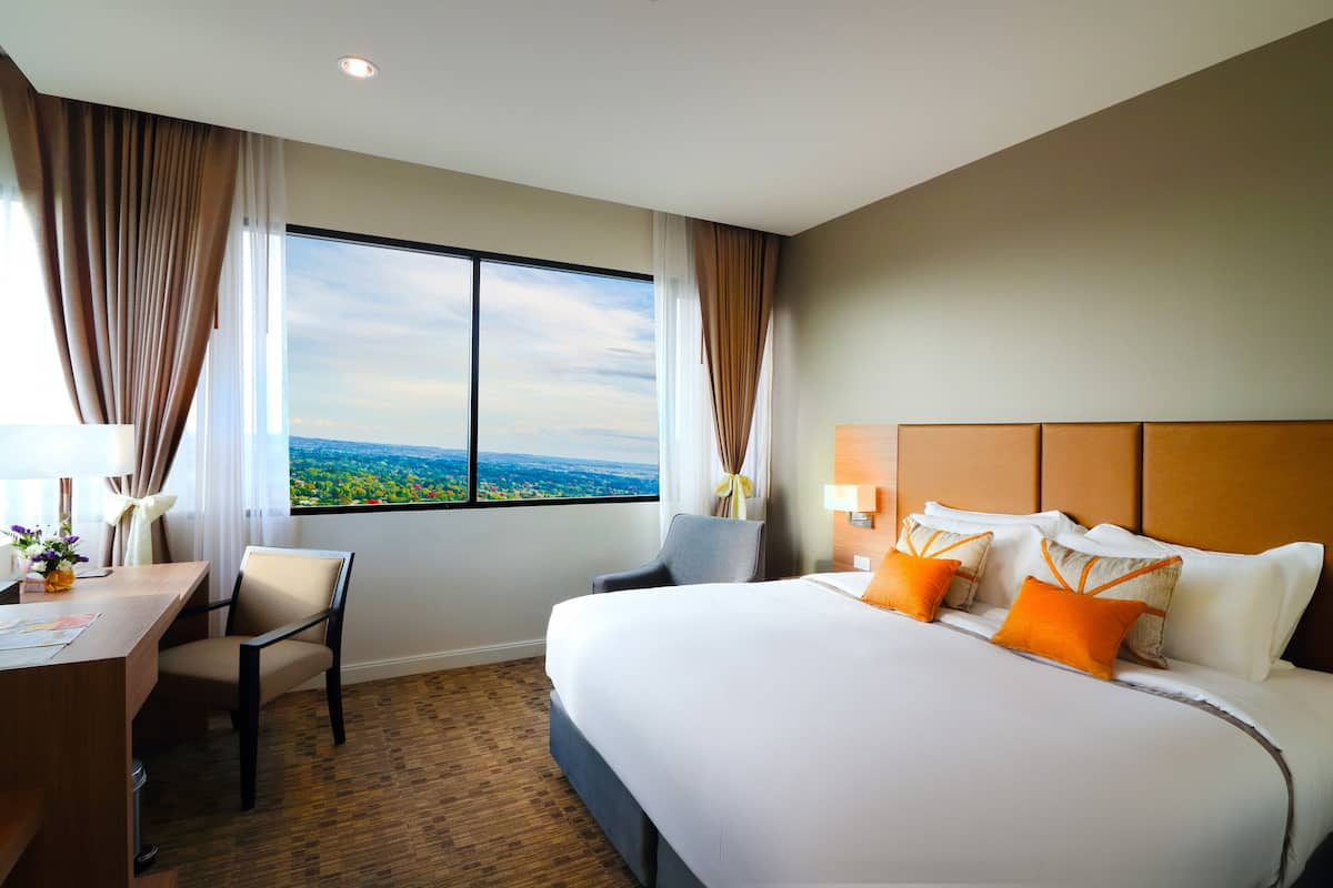 Quarto de hotel com uma cama grande, uma mesa e uma cadeira. Há uma janela com vista para a paisagem.