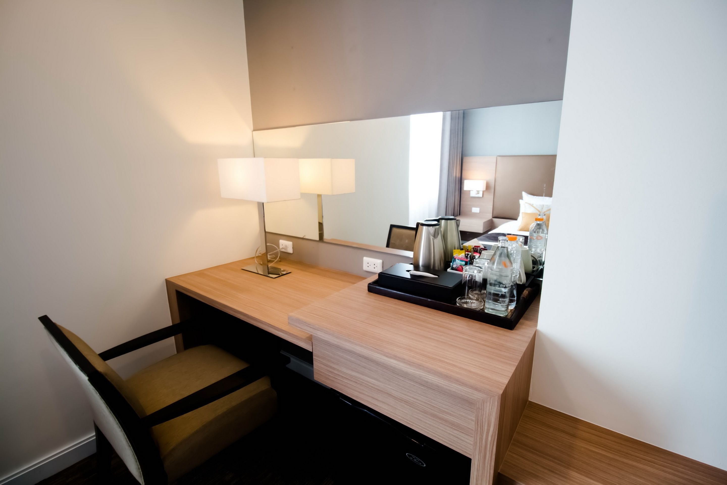 A hotel room with a wooden desk, a chair, a mirror, and a tray with toiletries.