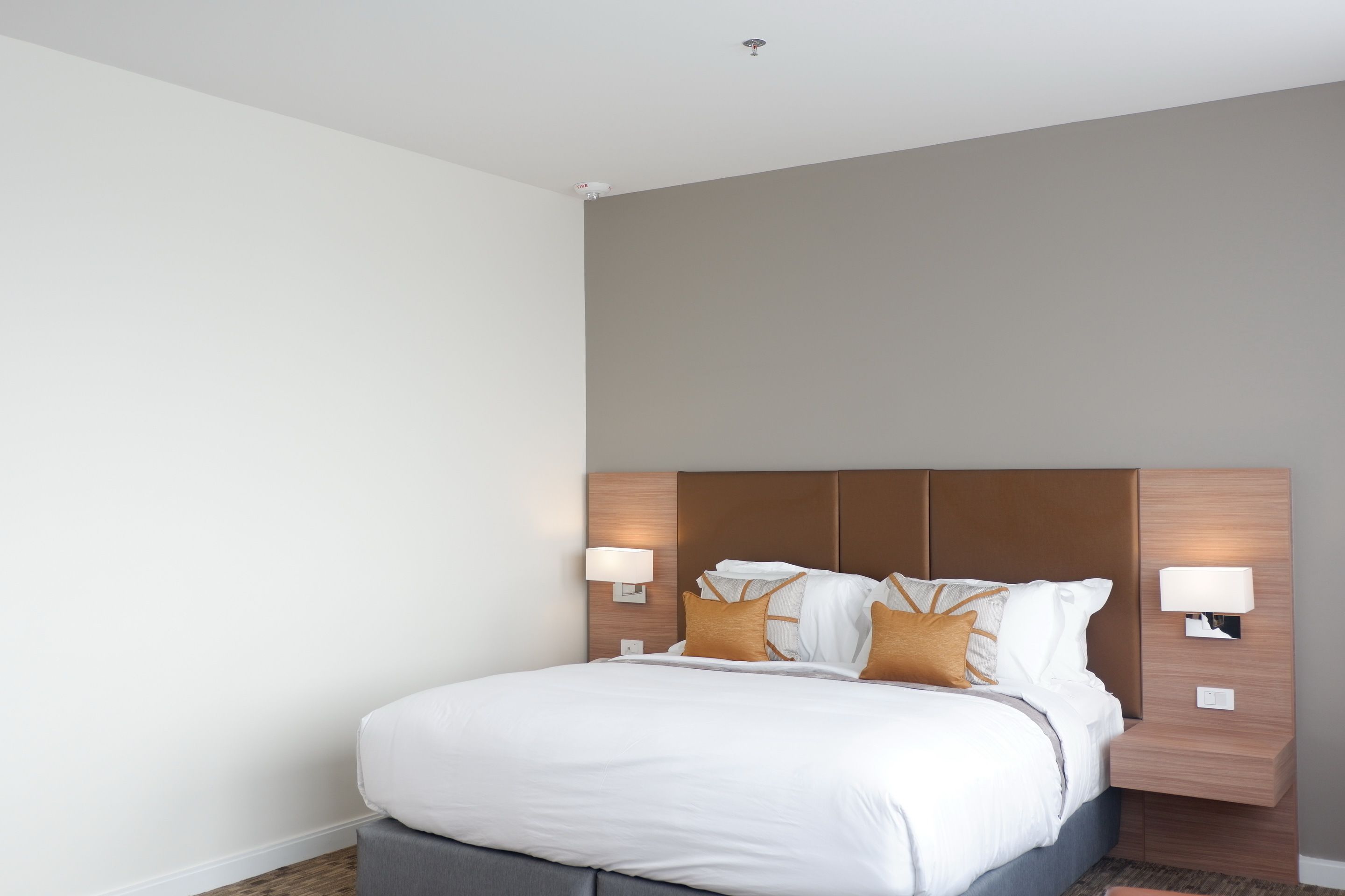 Une chambre d’hôtel moderne dotée d’un grand lit, de deux tables de chevet avec des lampes et d’une tête de lit avec un éclairage intégré.