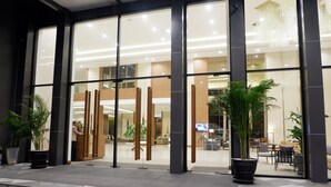 A modern hotel entrance with large glass doors, indoor seating area visible through the glass, and potted plants outside. - Grand Fortune Hotel Nakhon Si Thammarat (Nakhon Si Thammarat)