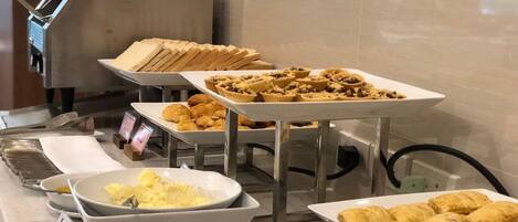 Un bufé con diferentes opciones de comida, incluyendo pasteles, pan y un bol de huevos revueltos.