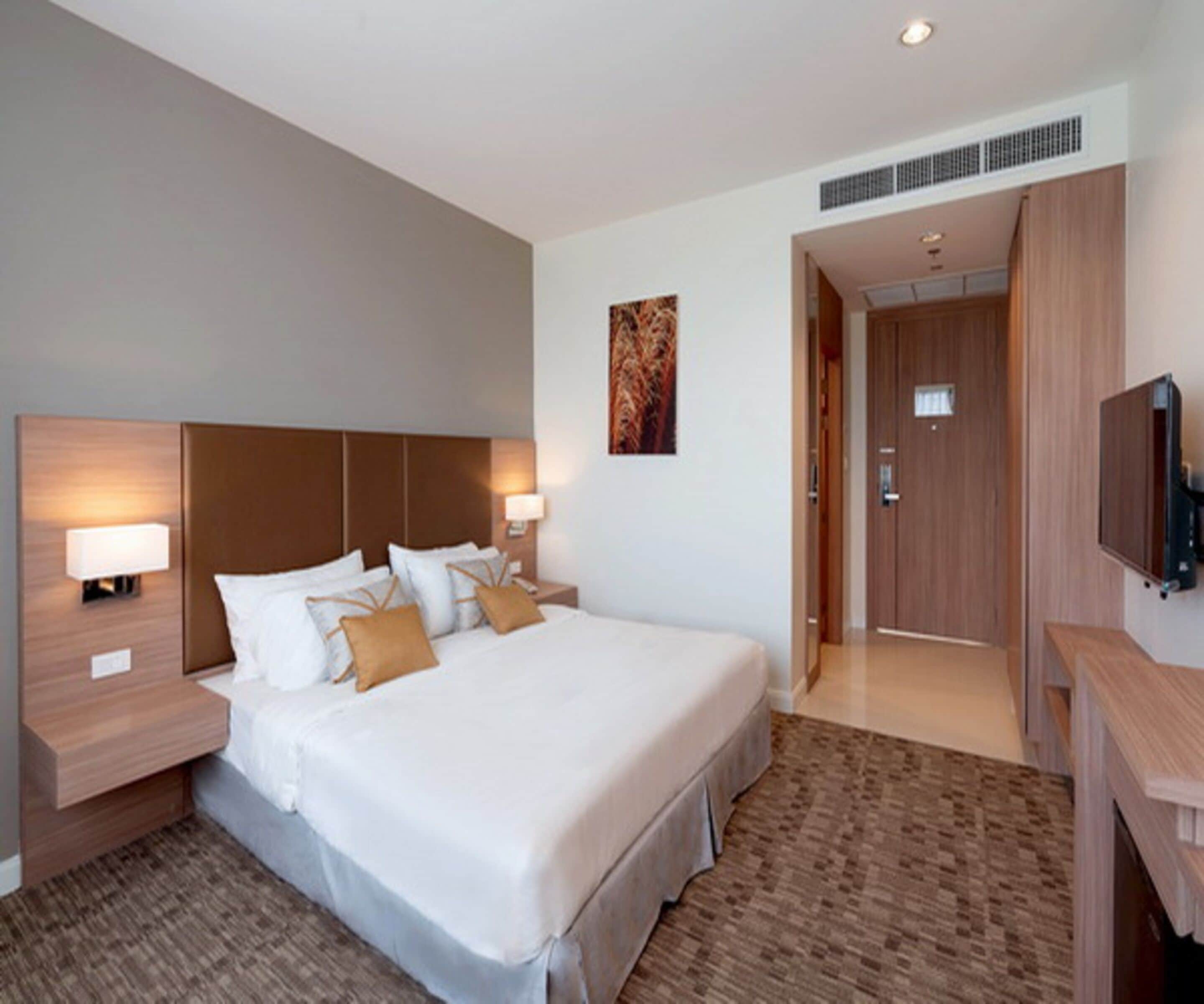 A hotel room with a large bed, bedside lamps, a flat-screen TV, and a door leading to another room.