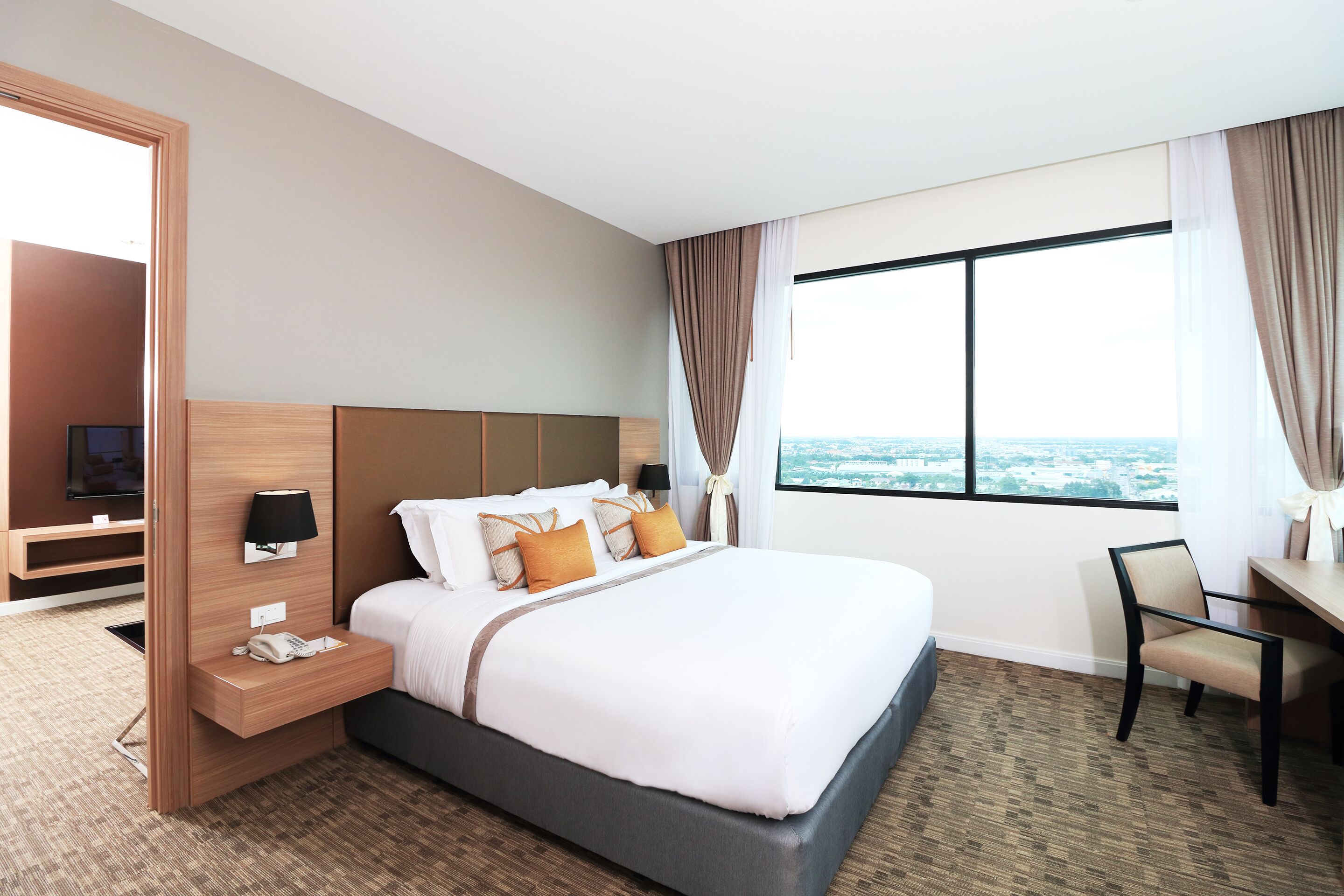 A modern hotel room with a large bed, a desk, and a view of the city.