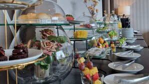 A buffet setup with various food items, including desserts and fruits, displayed on glass stands and under glass domes. - Grand Fortune Hotel Nakhon Si Thammarat (Nakhon Si Thammarat)