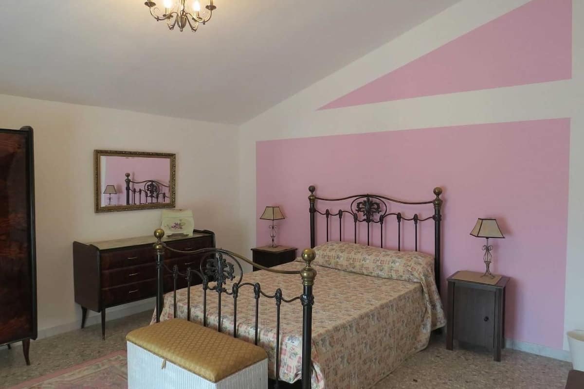 A bedroom with a bed, a dresser, a nightstand, a chair, and a chandelier.