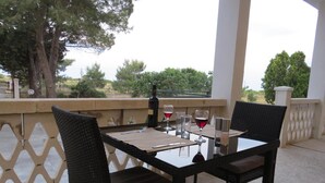 Un área de comedor al aire libre con una mesa lista para dos personas, una botella de vino y copas.