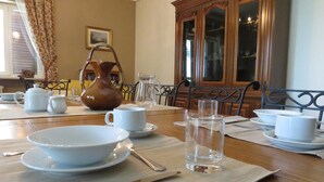 Una mesa de comedor dispuesta con platos, tazones y tazas blancos, una jarrón y un vaso de agua.