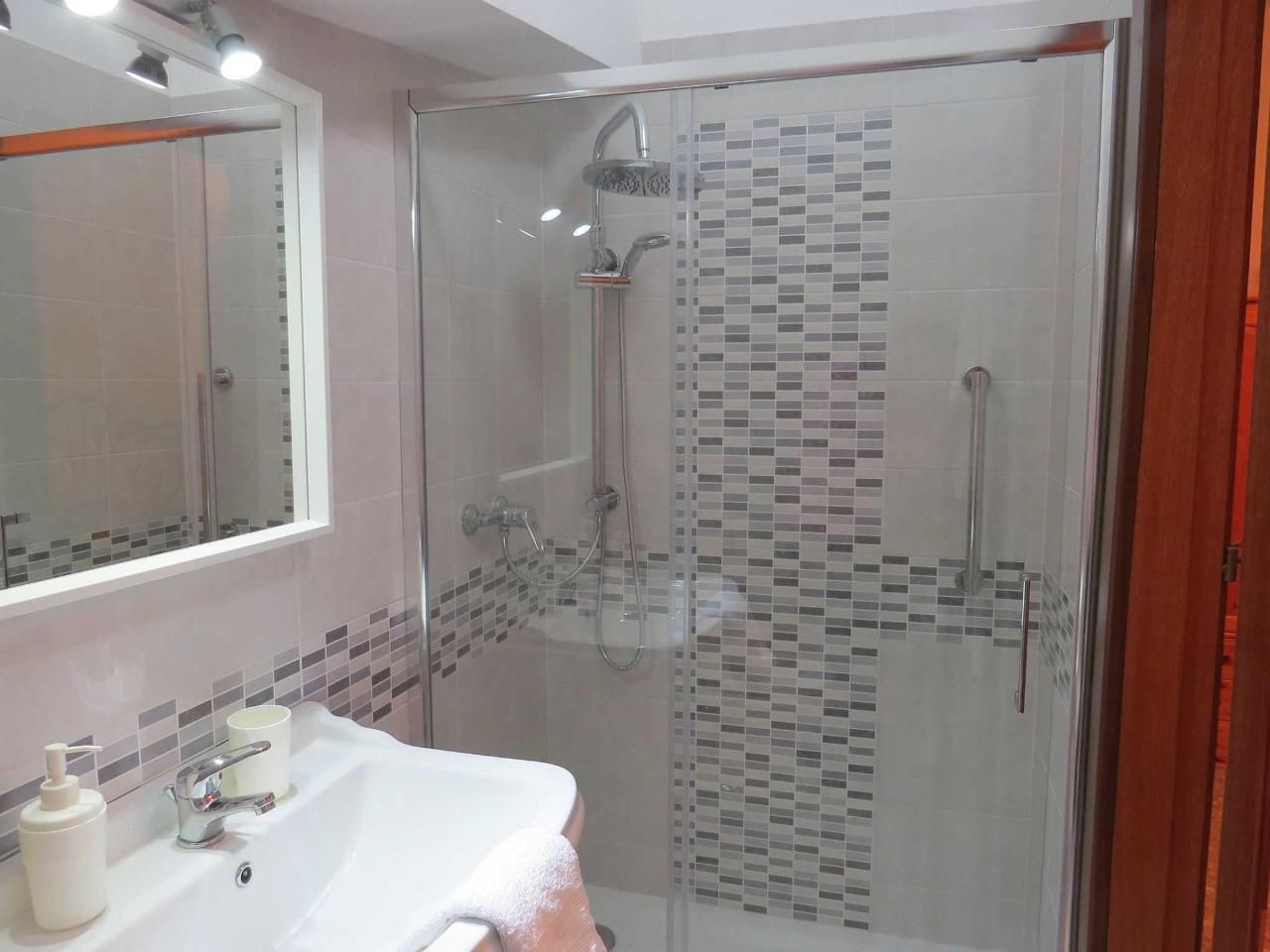 A bathroom with a glass-enclosed shower, a white sink with a mirror above it, and a tiled backsplash.
