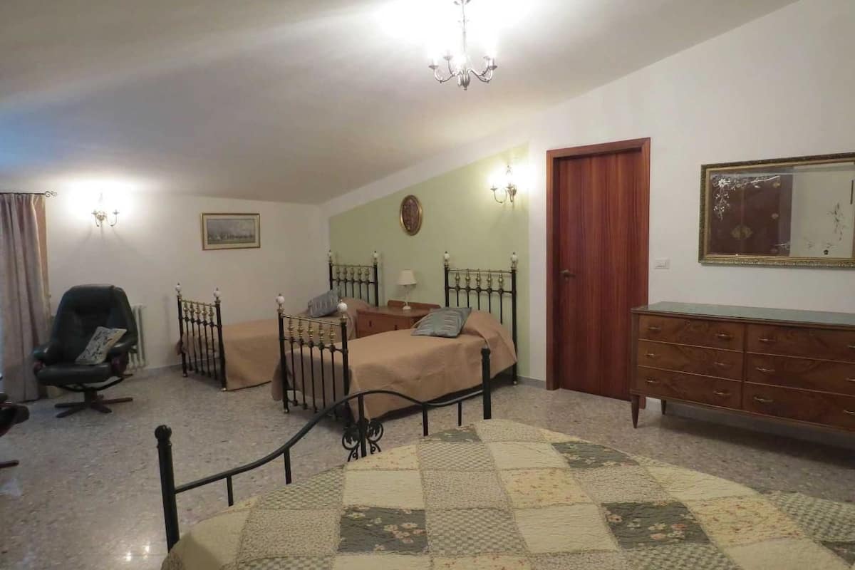 A bedroom with a bed, a chair, a dresser, a mirror, and a chandelier.