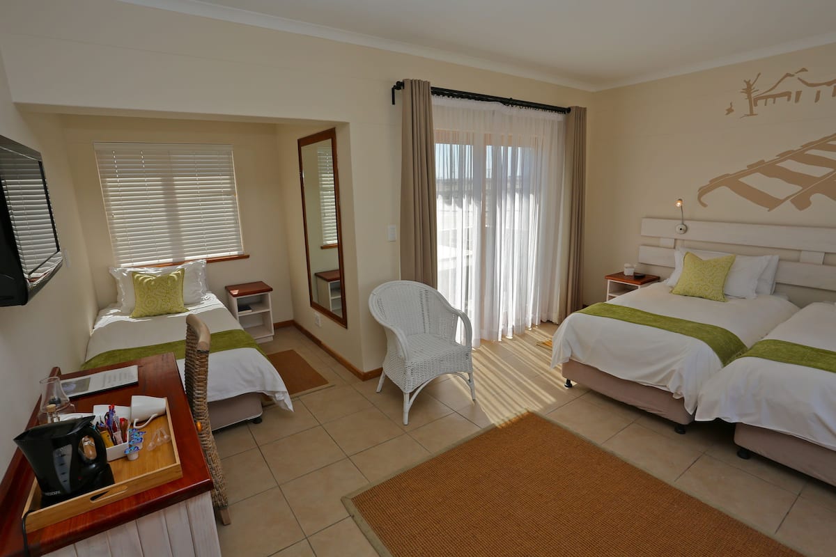 Une chambre d’hôtel avec deux lits, une chaise, un bureau avec un plateau et une fenêtre avec des stores.