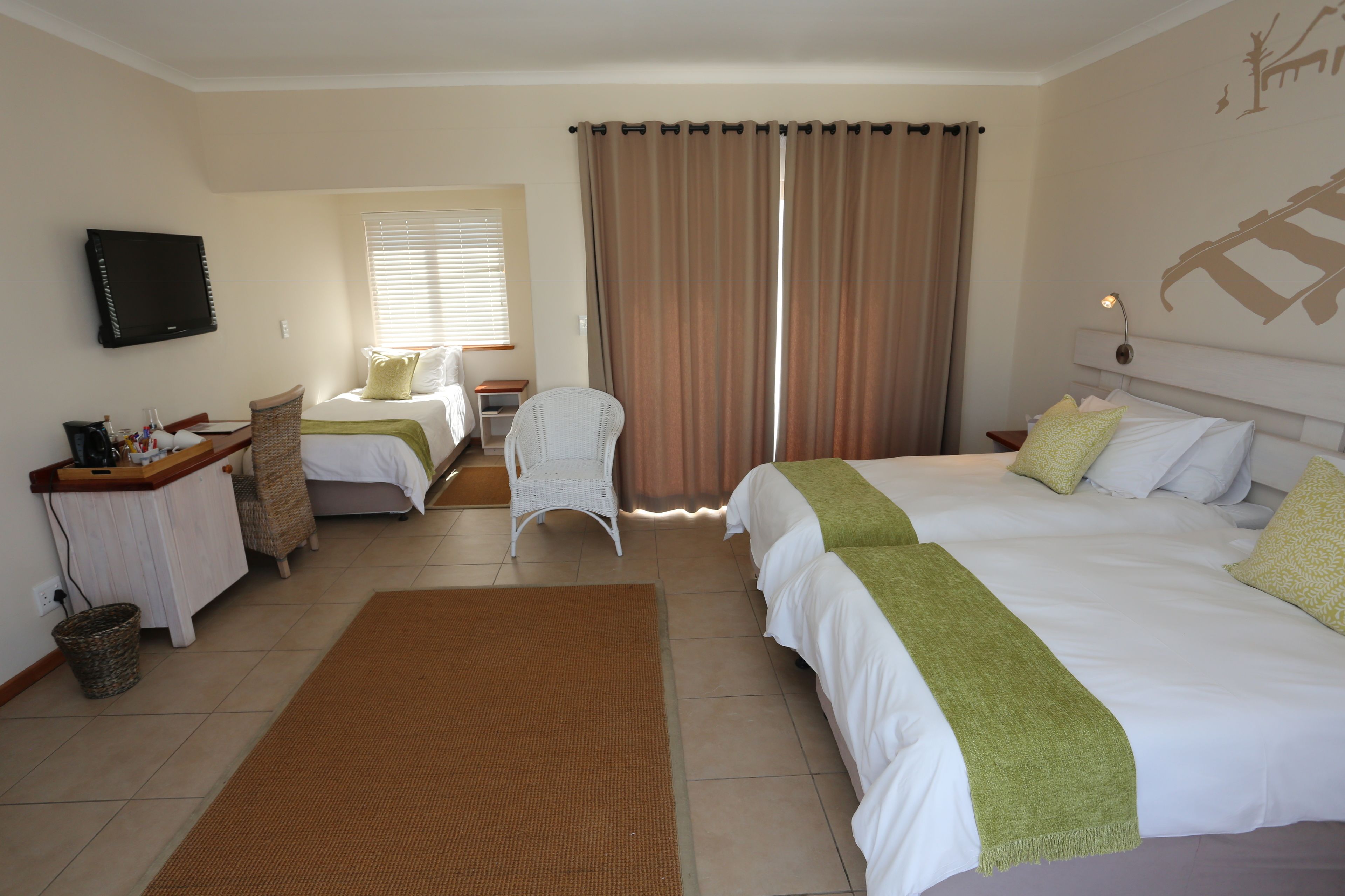 Habitación de hotel con dos camas, televisión, escritorio con silla y ventana con cortinas.