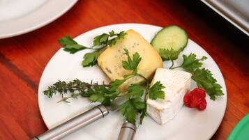 A plate with cheese, parsley, and a cucumber on a wooden table.